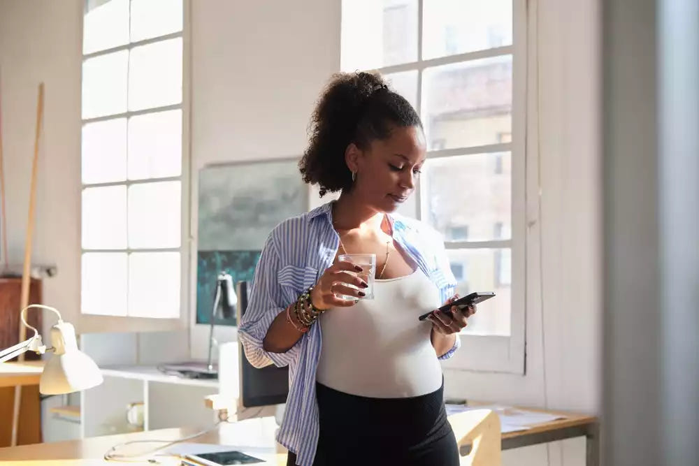 Pregnant woman standing near a window, holding a glass of water