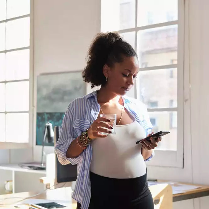Pregnant woman standing near a window, holding a glass of water