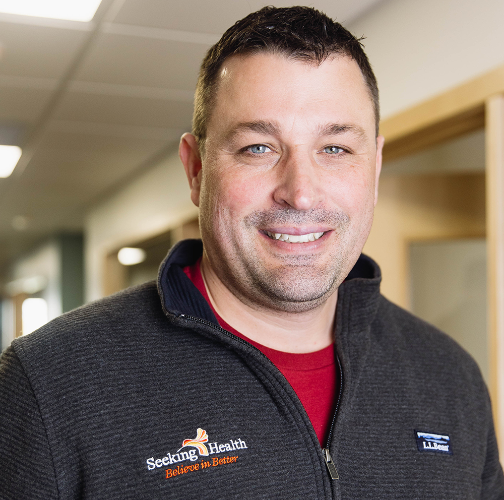 Man wearing a gray jacket with 'Seeking Health' logo in an indoor setting