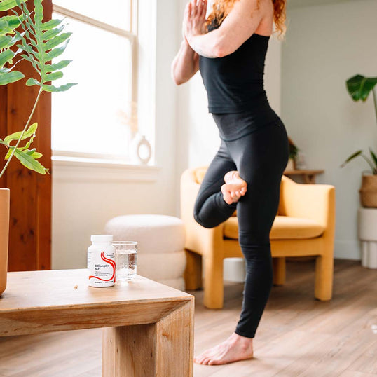 Person practicing yoga in a home setting with a supplement container on a table.
