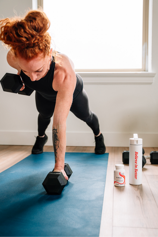 Woman exercising with dumbbells on a blue mat in a room with a window.