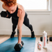 Woman exercising with dumbbells on a blue mat in a room with a window.