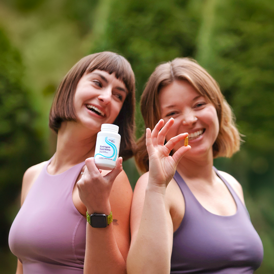 Two women outdoors holding a supplement bottle and a small object.