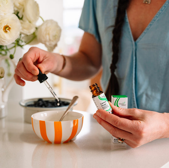 Person using a dropper with a bottle labeled 'Lactase Drops' on a table with flowers in the background.
