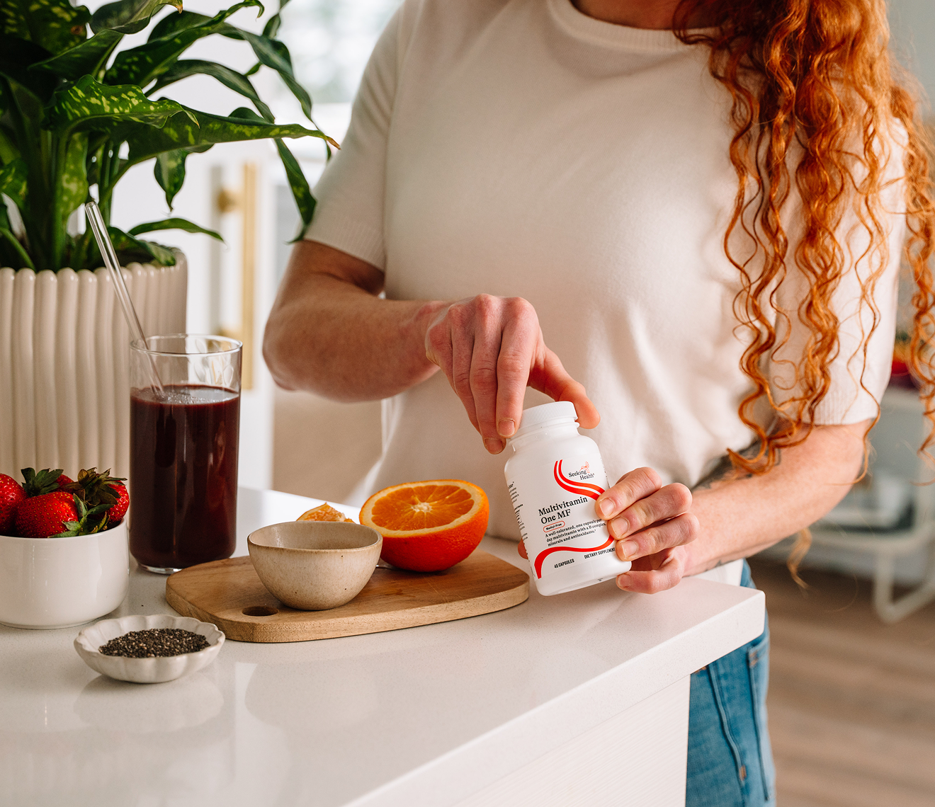 Person holding a supplement bottle in a kitchen setting with ingredients on the counter.