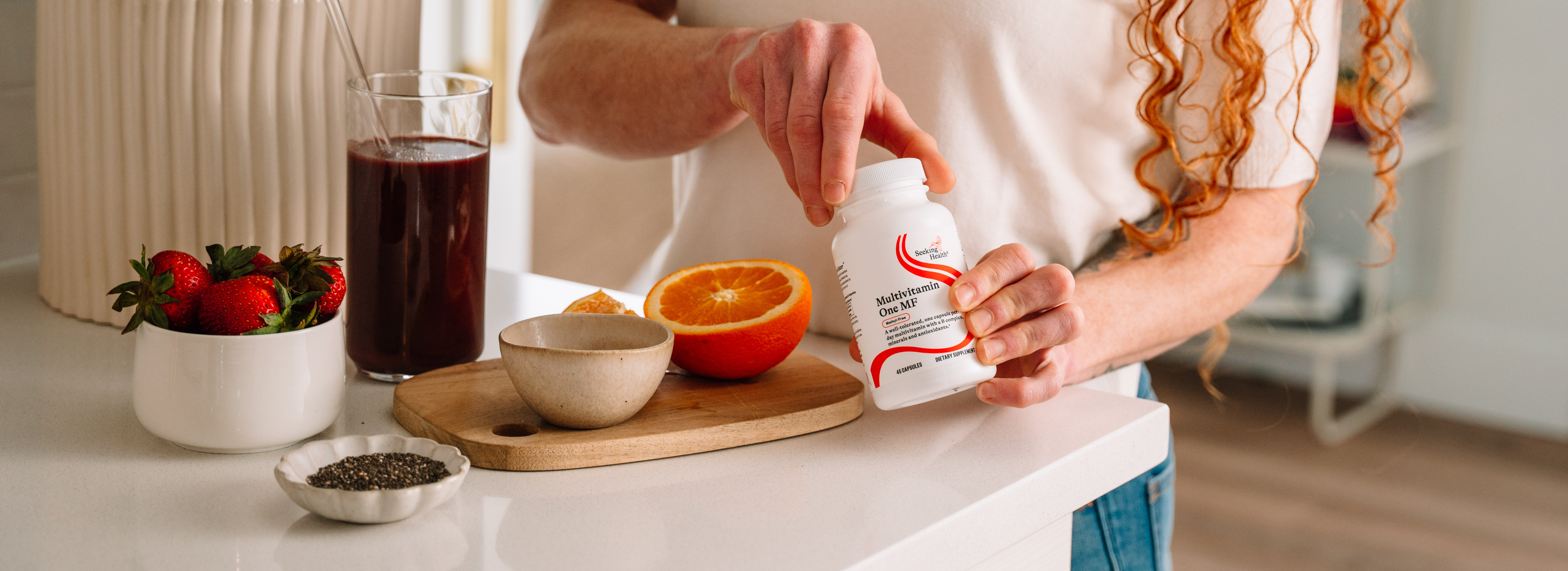 Person holding a supplement bottle with a kitchen counter in the background