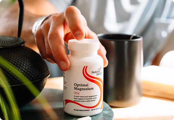 Hand holding a bottle of 'Optimal Magnesium' supplement with a blurred background