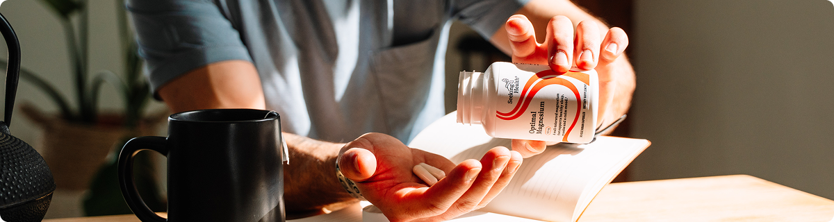 Person holding a bottle of pills with a cup and book in the background