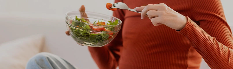 Person holding a bowl of salad and a fork with a blurred background